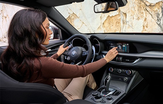 Kvinne sitter iførersete på en Stelvio og trykker på infotainmentskjerme på dashbordet