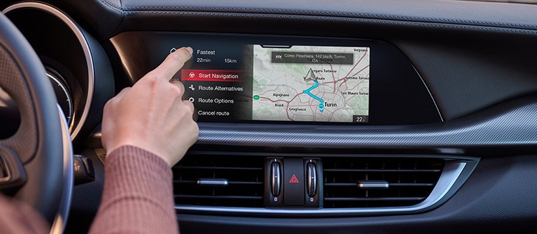hånd peker på en digital touchskjerm med kart på dashbordet til en Stelvio